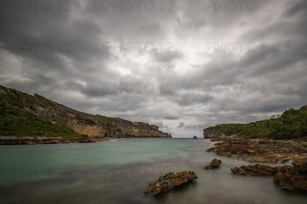 Rocky coast, long bay by the sea at sunset. Dangerous view of the Caribbean Sea. Tropical climate on a cloudy day in La Porte d'Enfer, Grande Terre, Guadeloupe, French Antilles, North America