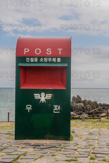 Close-up of a red and green mailbox with Korean text against a sea backdrop, in Ulsan, South Korea, Asia