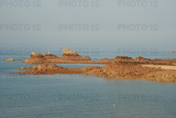 A tranquil seascape with rocks emerging from calm blue waters under a clear sky