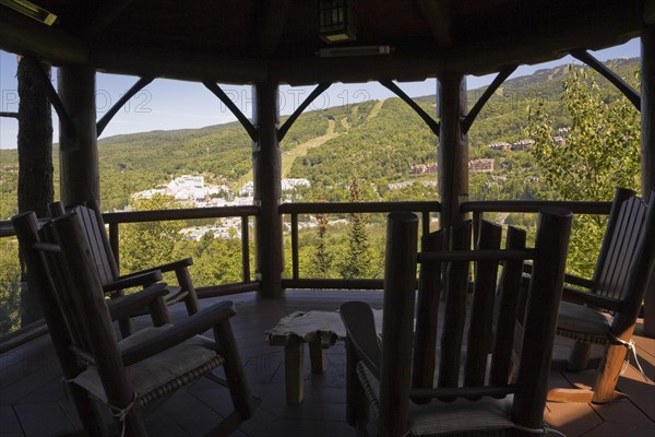 Brown stained gazebo on wooden deck with tempered glass and log railings attached to back of luxurious log cabin home overlooking Mt-Tremblant ski resort in summer, Quebec, Canada, North America