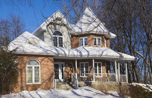 Two story red brick Victorian style home with white trim and landscaped front yard in winter, Quebec, Canada, North America