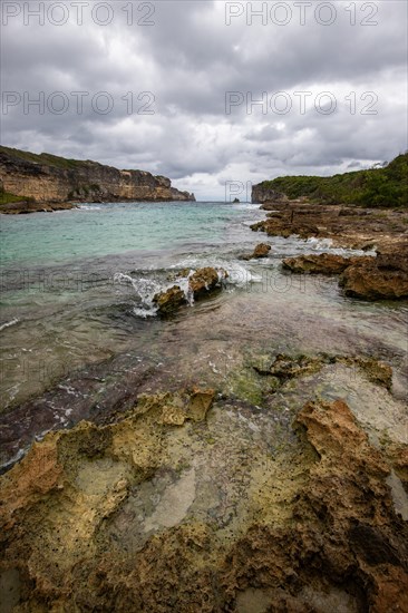 Rocky coast, long bay by the sea at sunset. Dangerous view of the Caribbean Sea. Tropical climate on a cloudy day in La Porte d'Enfer, Grande Terre, Guadeloupe, French Antilles, North America