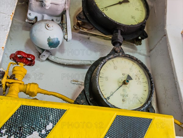 Old pressure gauges mounted above yellow and black striped ledge with valves and bell in background in Gangneung, South Korea, Asia