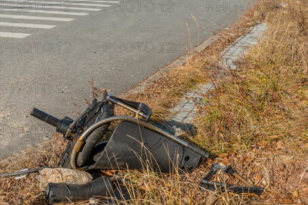 Broken office chair dumped on the side of a road amidst weeds and grass, in South Korea