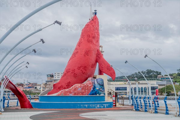 Red sculpture dominating the harbor space with boats and blue railings under a cloudy sky, in Ulsan, South Korea, Asia