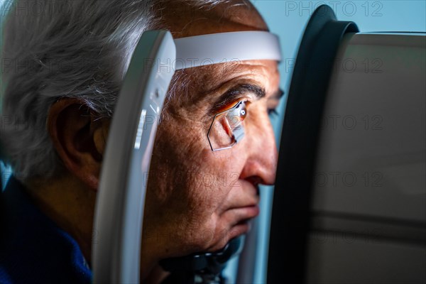 Close-up photo of a serious senior man with eye opener looking through an innovative machine during a laser treatment for glaucoma