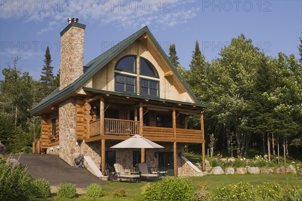 Handcrafted two story spruce log home cabin with fieldstone chimney and green sheet metal roof in summer, Quebec, Canada, North America