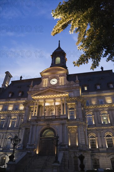 Second empire style multistory Montreal City Hall building facade with lights on at dusk, Old Montreal, Quebec, Canada, North America