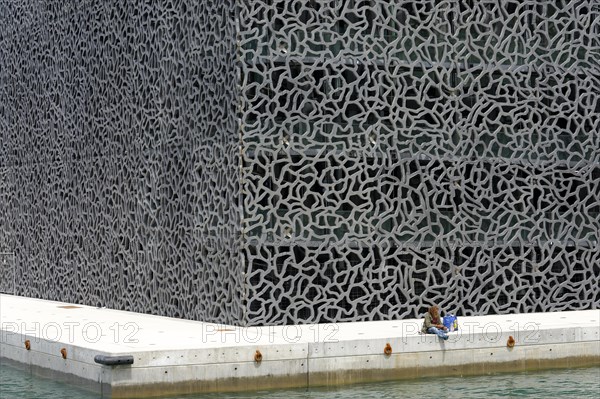 Marseille, Person sitting lonely on the quay wall in front of a wall with extraordinary texture, Marseille, Departement Bouches-du-Rhone, Region Provence-Alpes-Cote d'Azur, France, Europe