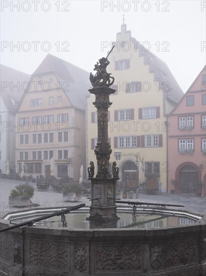 The market square with town houses and St George's Fountain in the historic old town in the morning mist, Rothenburg ob der Tauber, Middle Franconia, Bavaria, Germany, Europe