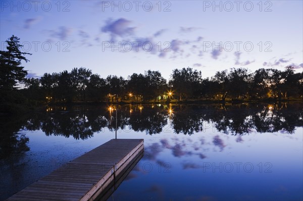 Wooden dock floating on calm surface of Mille-Iles river and view of Ile des Moulins illuminated at dawn, Old Terrebonne, Lanaudiere, Quebec, Canada, North America
