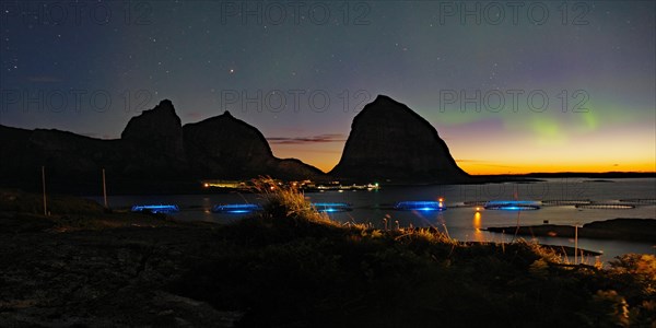 Northern lights (aurora borealis) mingle with sunset, sea, striking mountains and fish farm, Lovunden, Helgeland coast, Traena, Norway, Europe