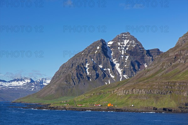 Rugged mountains and orange lighthouse at Skalanes along the fjord Seyoisfjoerour, Seydisfjoerdur in summer, Eastern Region, Austurland, Iceland, Europe