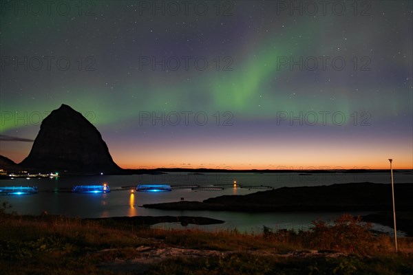 Northern lights (aurora borealis) mingle with sunset, sea, striking mountains and fish farm, Lovunden, Helgeland coast, Traena, Norway, Europe