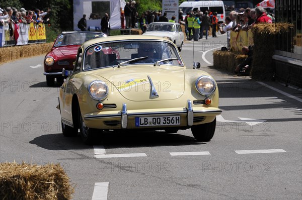 A yellow vintage sports car takes part in a street race, surrounded by spectators, SOLITUDE REVIVAL 2011, Stuttgart, Baden-Wuerttemberg, Germany, Europe