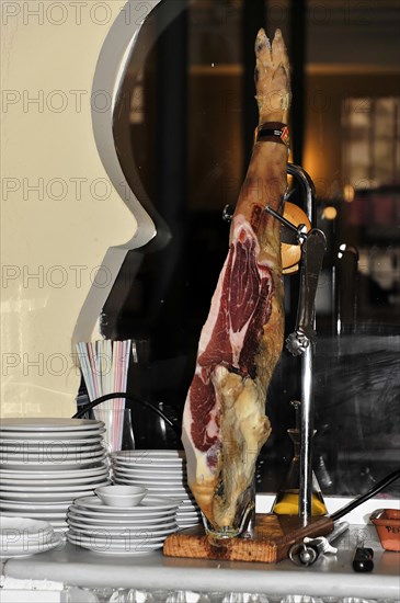 Jaen, A Jamon Iberico on a wooden board next to a pile of plates in a restaurant, Jaen, Andalusia, Spain, Europe