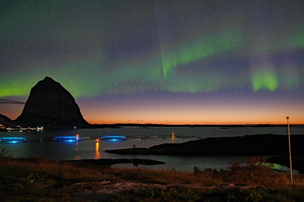Northern lights (aurora borealis) mingle with sunset, sea, striking mountains and fish farm, Lovunden, Helgeland coast, Traena, Norway, Europe