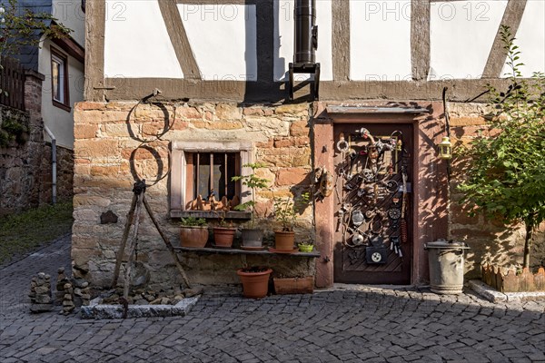 Old half-timbered house, whimsically decorated, stone towers, tripod with pendulum, flower pots, door with masks, skulls, engine parts, cartridge cases, tools, old town, Ortenberg, Vogelsberg, Wetterau, Hesse, Germany, Europe