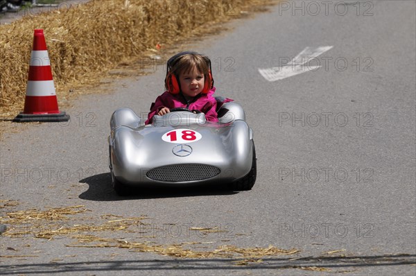 A young child in a silver soapbox smilingly drives past bales of straw, SOLITUDE REVIVAL 2011, Stuttgart, Baden-Wuerttemberg, Germany, Europe