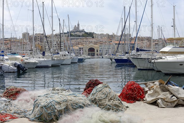 Marseille harbour, Colourful sailing boats and fishing boats in the harbour, red fishing nets in the foreground, church in the background, Marseille, Departement Bouches-du-Rhone, Region Provence-Alpes-Cote d'Azur, France, Europe