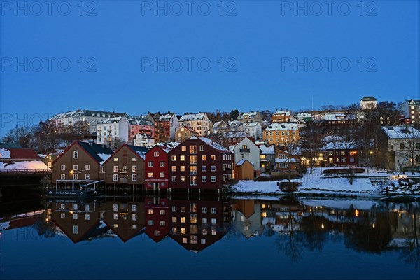 Historic warehouse buildings reflected in the river Nidelva at dusk, Bryggene, Trondheim, Norway, Europe