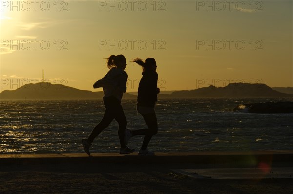 Marseille in the evening, Two joggers run along the sea at sunset, their silhouettes stand out, Marseille, Departement Bouches-du-Rhone, Region Provence-Alpes-Cote d'Azur, France, Europe