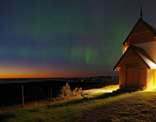Northern lights (aurora borealis) merging with sunset, Petter Dass Chapel, night shot, Lovunden, Helgeland coast, Traena, Norway, Europe