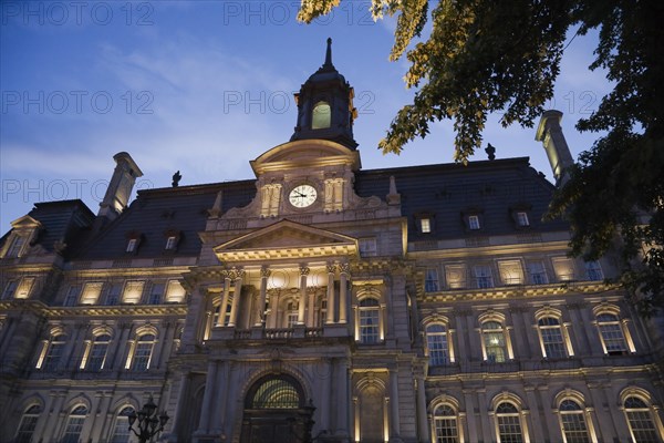 Second empire style multistory Montreal City Hall building facade with lights on at dusk, Old Montreal, Quebec, Canada, North America