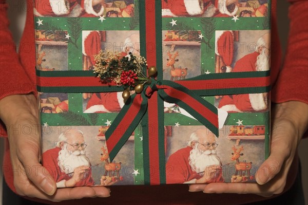 Close-up of woman's arms and hands holding and offering a boxed Christmas gift, Studio Composition, Quebec, Canada. This image is model released. MR0129