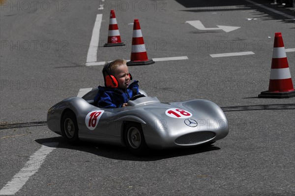Smiling child enjoying a ride in a silver soapbox on a closed-off road, SOLITUDE REVIVAL 2011, Stuttgart, Baden-Wuerttemberg, Germany, Europe