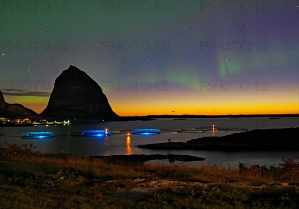 Northern lights (aurora borealis) mingle with sunset, sea, striking mountains and fish farm, Lovunden, Helgeland coast, Traena, Norway, Europe