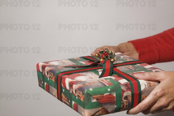 Close-up of extended woman's hands holding and offering a wrapped Christmas gift, Studio Composition, Quebec, Canada. This image is model released. MR0129