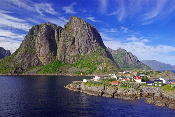 Rough rocks and small huts on a rocky headland jutting into a fjord, Reine, Reinefjord, Lofoten, Nordland, Norway, Europe
