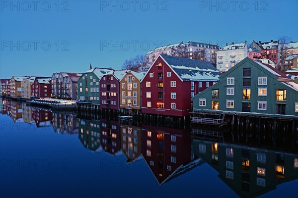 Historic warehouse buildings reflected in the river Nidelva at dusk, Bryggene, Trondheim, Norway, Europe