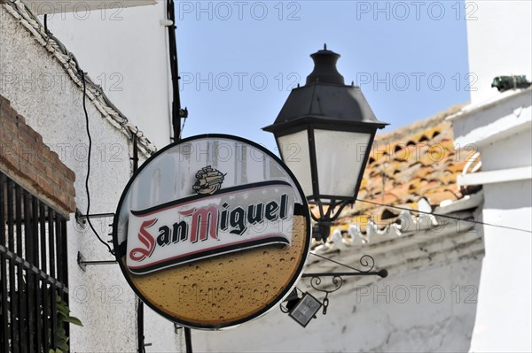 Solabrena, A round beer advertising sign for San Miguel on a wall next to a lantern, Andalusia, Spain, Europe
