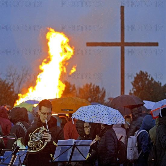 Musicians with a double horn in front of the Easter bonfire on the Haniel spoil tip with the summit cross in the rain, Bottrop, Ruhr area, Germany, Europe