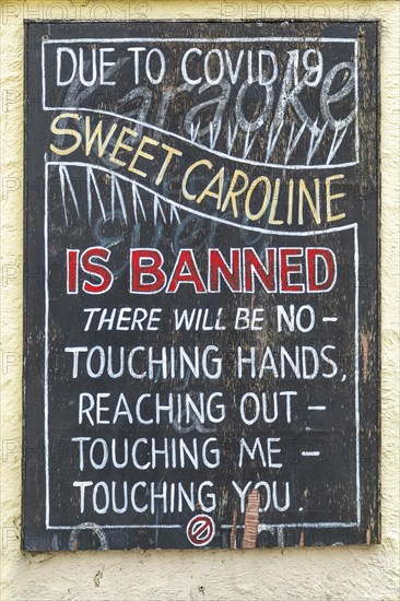 Sign outside pub advising that handshaking and touching is prohibited during the song Sweet Caroline due to Covid 19, Holyhead, Isle of Anglesey, Wales, United Kingdom, Europe