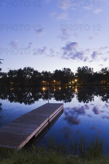 Wooden dock floating on calm surface of Mille-Iles river and view of Ile des Moulins illuminated at dawn, Old Terrebonne, Lanaudiere, Quebec, Canada, North America