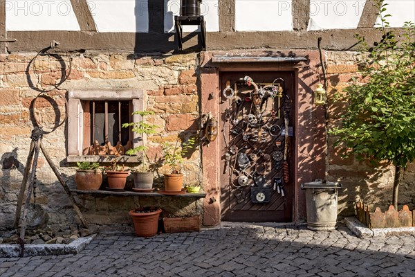 Old half-timbered house, whimsically decorated, tripod with pendulum, flower pots, door with masks, skulls, engine parts, cartridge cases, tools, old town, Ortenberg, Vogelsberg, Wetterau, Hesse, Germany, Europe