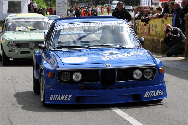 A blue BMW racing car with Gitanes branding at a road race, surrounded by spectators, SOLITUDE REVIVAL 2011, Stuttgart, Baden-Wuerttemberg, Germany, Europe