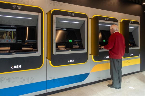 Elderly man collecting money from indoor ATM cash dispenser of bank neutral Bancontact CASH point in Flanders, Belgium. MODEL RELEASED