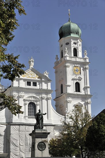St Stephan Cathedral, Passau, White baroque church with high tower and a statue in the foreground, against blue sky, Passau, Bavaria, Germany, Europe
