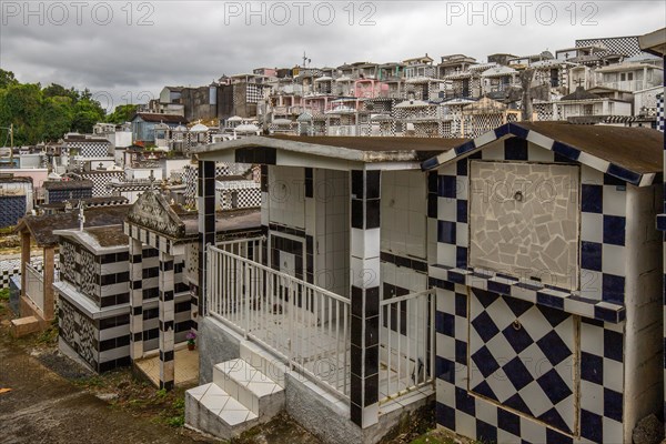 Famous cemetery, many mausoleums or large tombs decorated with tiles, often in black and white. Densely built buildings under a dramatic cloud cover Cimetiere de Morne-a-l'eau, Grand Terre, Guadeloupe, Caribbean, North America