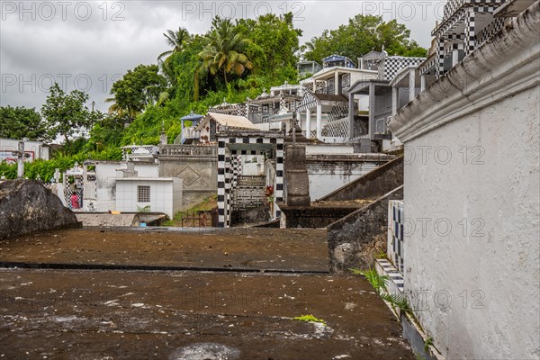 Famous cemetery, many mausoleums or large tombs decorated with tiles, often in black and white. Densely built buildings under a dramatic cloud cover Cimetiere de Morne-a-l'eau, Grand Terre, Guadeloupe, Caribbean, North America