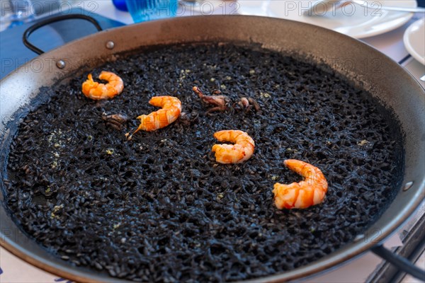 Black rice with prawns and squid, a dry rice, cooked in paella or in a clay pot, a characteristic flavor of Valencian Mediterranean cuisine. Spain