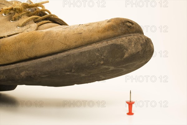 Close-up of elevated old and worn safety work shoe about to step on red upright pushpin with sharp point on white background, Studio Composition, Quebec, Canada, North America