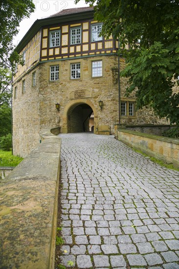 Access to the moated castle Sachsenheim, Grosssachsenheim Castle, former moated castle, archway, cobblestones, path, wall, bridge, crossing, stone figure on the left, relief of the legendary figure Klopferle, castle ghost, coat of arms, with inscription, exterior lights, lamps, architecture, historical building from the 15th century, Sachsenheim, Ludwigsburg district, Baden-Wuerttemberg, Germany, Europe
