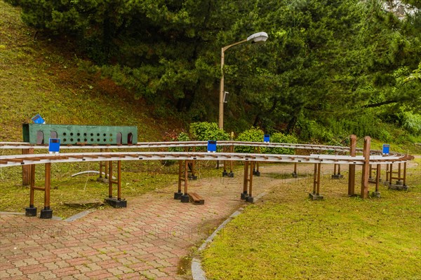 Miniature outdoor train station with benches and lampposts surrounded by trees on a cloudy day, in South Korea