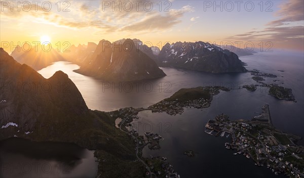 Mountain landscape, view from Reinebringen mountain to the village of Reine and Gravdalsbukta (Gravdals Bay), Olstinden mountain in the centre, Lilandstinden mountain on the right. On the left the Reinefjord with other mountains. At night at the time of the midnight sun in good weather. The sun is above the mountains. Early summer. Panoramic shot. Reine, Moskenesoya, Lofoten, Norway, Europe