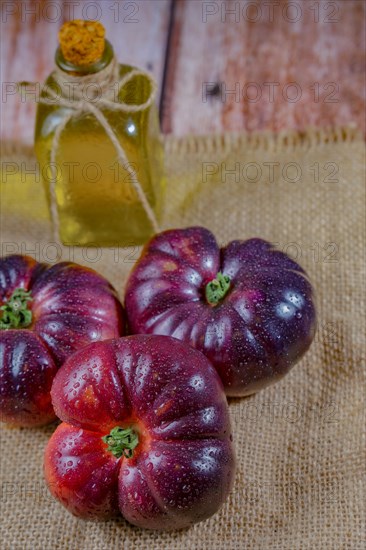 Group of tasty fresh tomatoes of the blue variety on a burlap cloth with a bottle of olive oil in the background